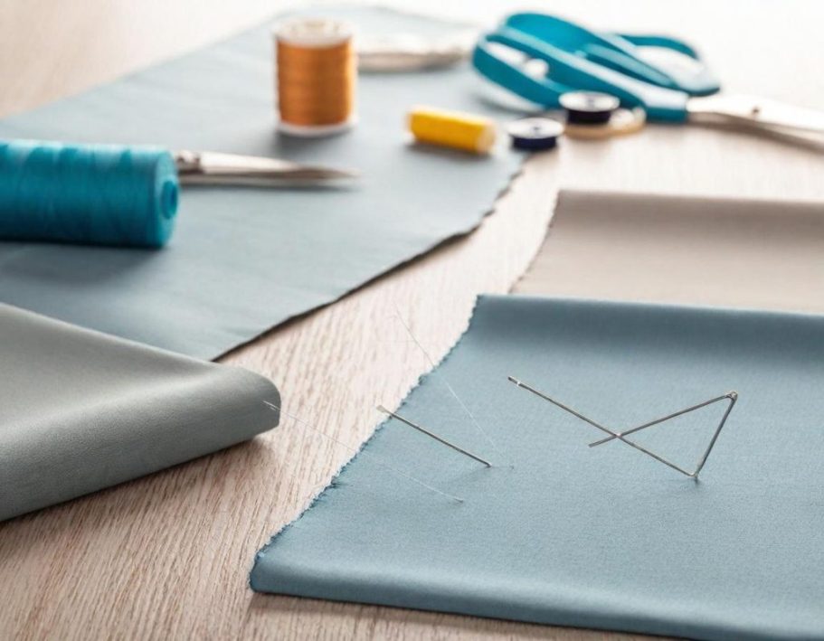 Zwei blaue Stoffstücke mit Scheren, Nähgarn und Nadel auf einem Tisch.